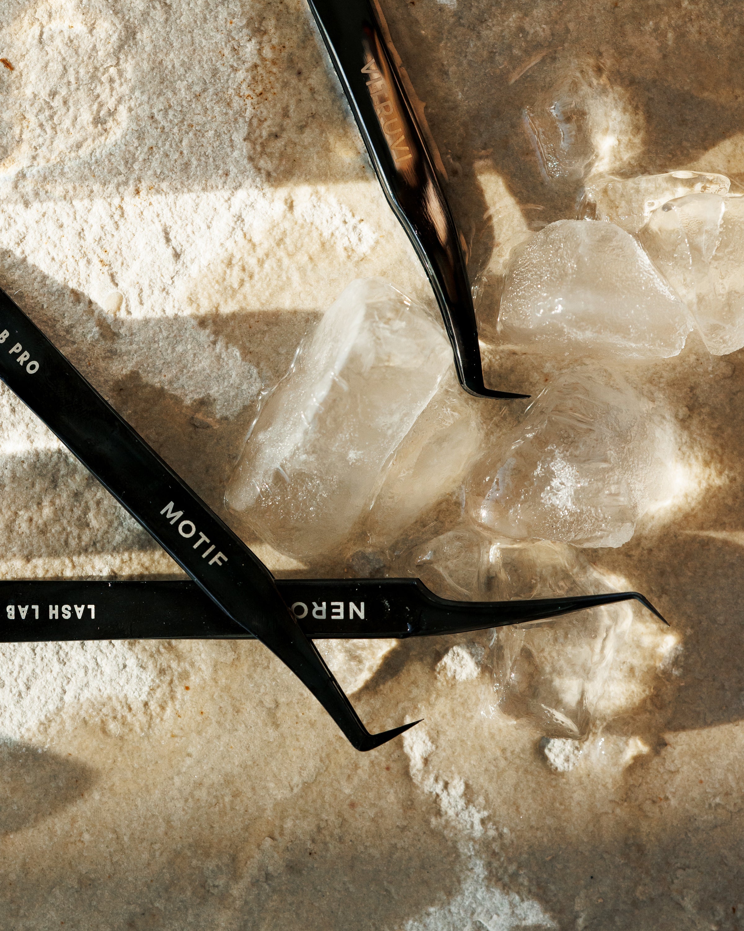 Black eyelash extensions tweezer on a stone surface with ice